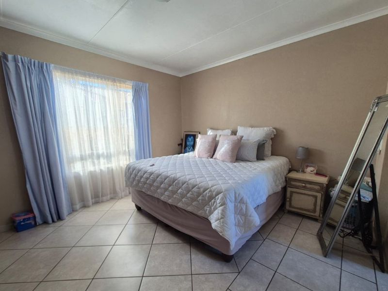 A spacious bedroom featuring neutral wall tones, large window with natural light, and durable tiled flooring throughout.