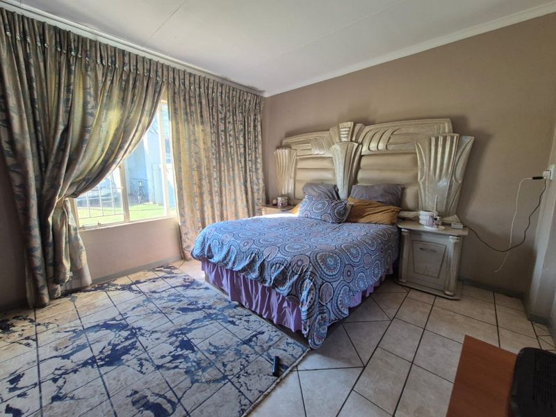 A spacious bedroom featuring tiled flooring and a large window with floor-to-ceiling curtains, offering a neutral canvas for potential updates.