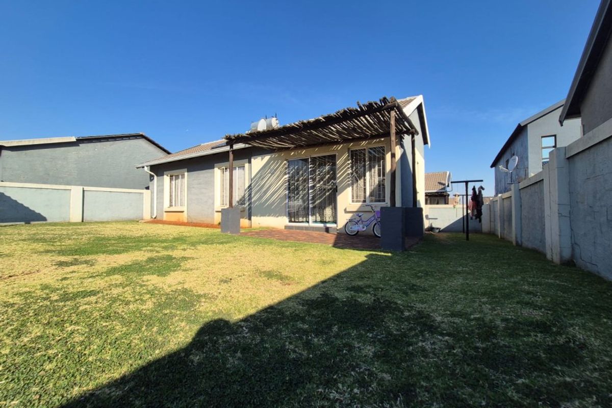 Rear view of the house featuring a paved patio with a rustic thatched pergola, sliding door access, and a private enclosed garden area.