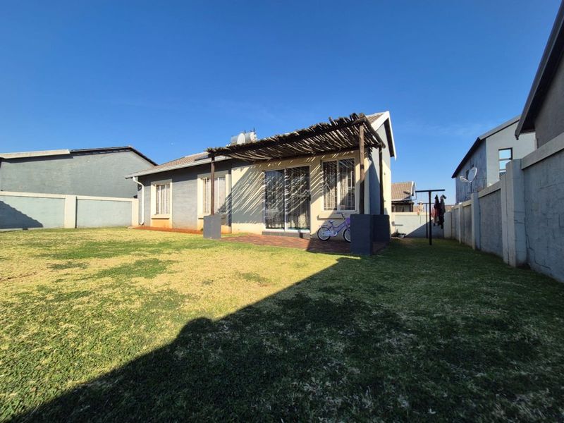 Rear view of the house featuring a paved patio with a rustic thatched pergola, sliding door access, and a private enclosed garden area.