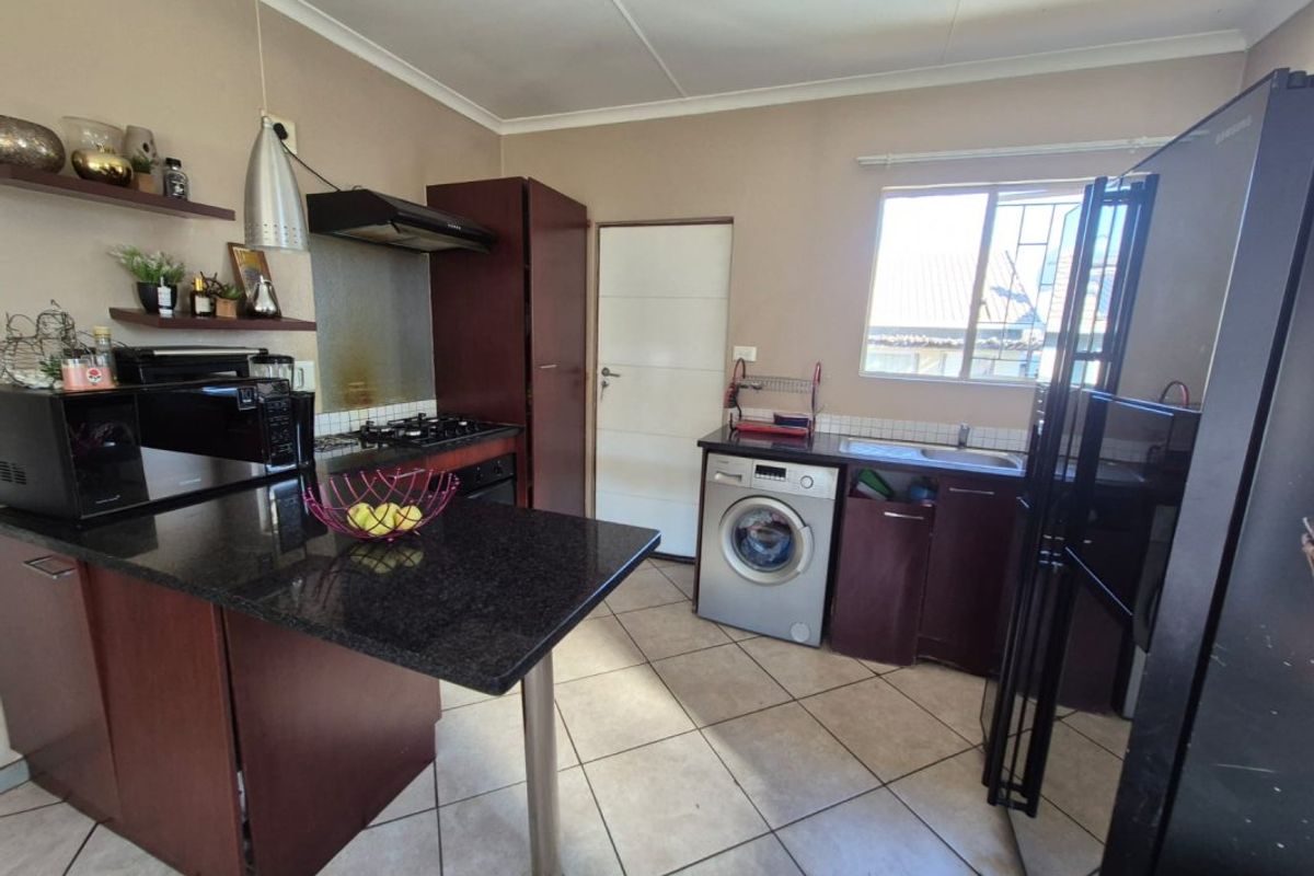 Functional kitchen featuring dark cabinetry, granite countertops, gas hob with extractor, and integrated laundry space with tiled flooring.