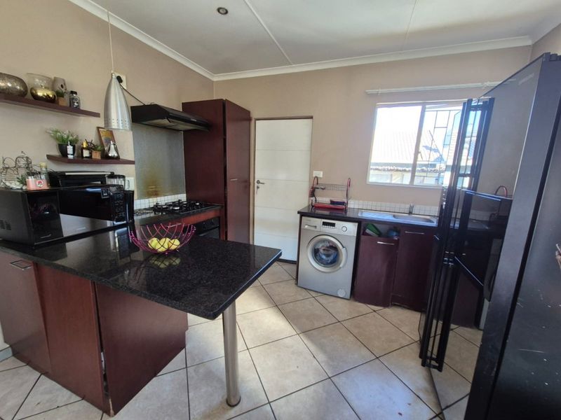 Functional kitchen featuring dark cabinetry, granite countertops, gas hob with extractor, and integrated laundry space with tiled flooring.