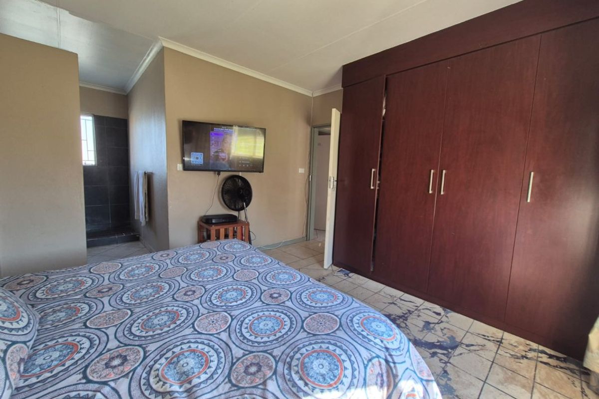 A bedroom featuring built-in wooden cupboards, tiled flooring, and direct access to an en-suite bathroom area.