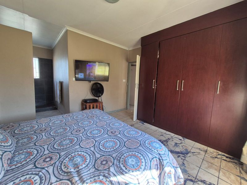 A bedroom featuring built-in wooden cupboards, tiled flooring, and direct access to an en-suite bathroom area.