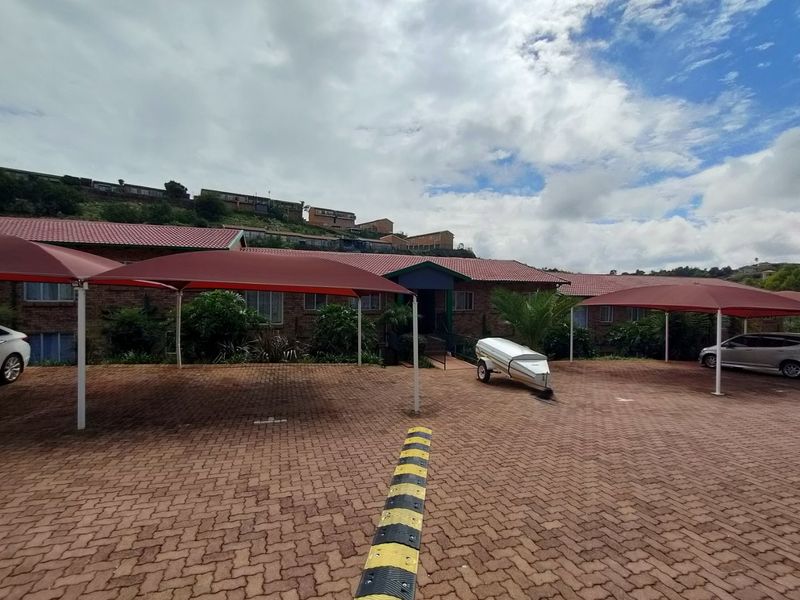 Exterior view of the apartment complex featuring a paved parking area with covered carports and brick building facades.
