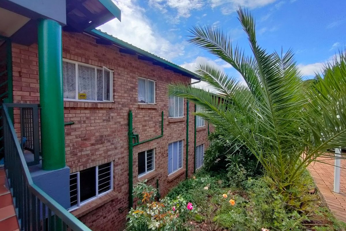 Exterior view of a multi-story face brick apartment building featuring a balcony with metal railings and landscaped garden area.
