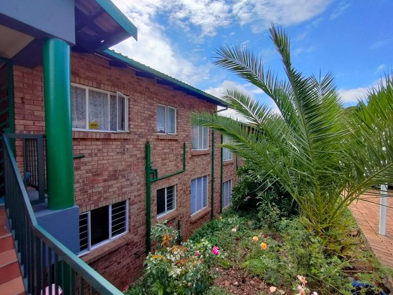 Exterior view of a multi-story face brick apartment building featuring a balcony with metal railings and landscaped garden area.
