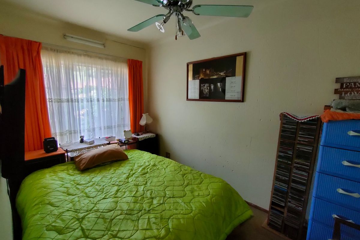 A bedroom featuring a ceiling fan and large window with curtain rails, showing signs of wear on the wall surfaces.