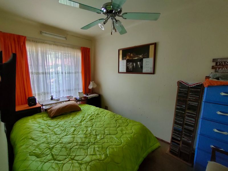 A bedroom featuring a ceiling fan and large window with curtain rails, showing signs of wear on the wall surfaces.