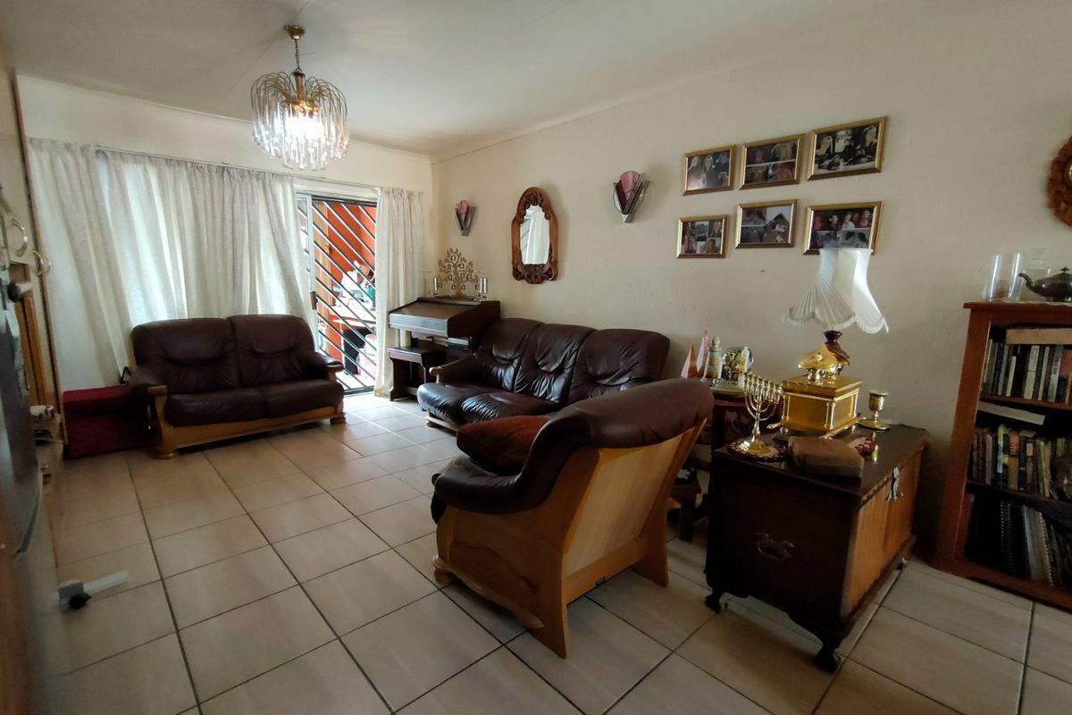 A spacious living room featuring neutral tiled flooring, a central light fixture, and a sliding glass door providing access to the exterior.