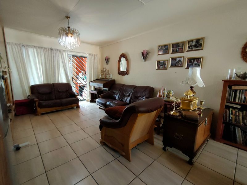 A spacious living room featuring neutral tiled flooring, a central light fixture, and a sliding glass door providing access to the exterior.