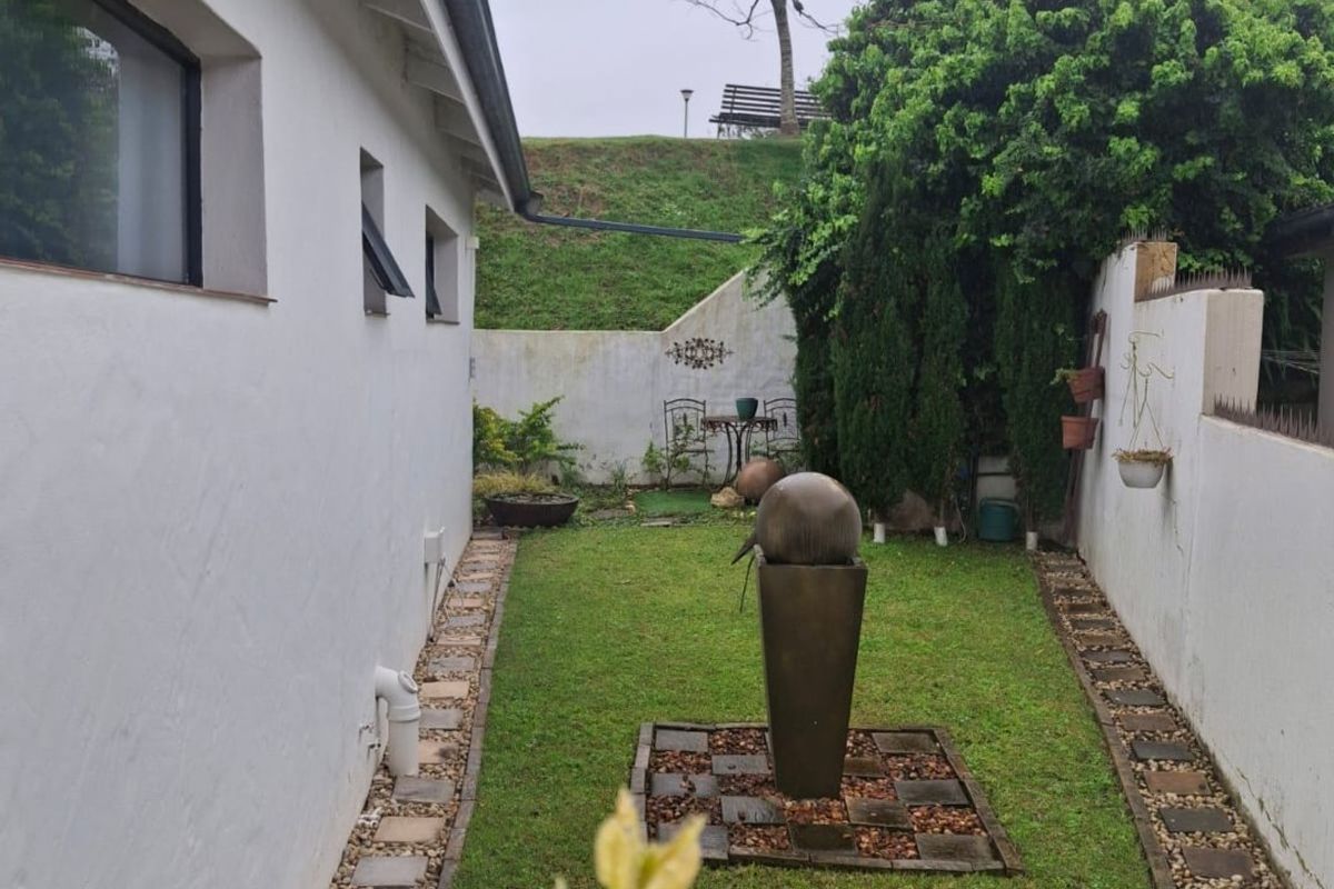 A private rear garden featuring a central water feature, manicured lawn, and paved pathways enclosed by boundary walls.