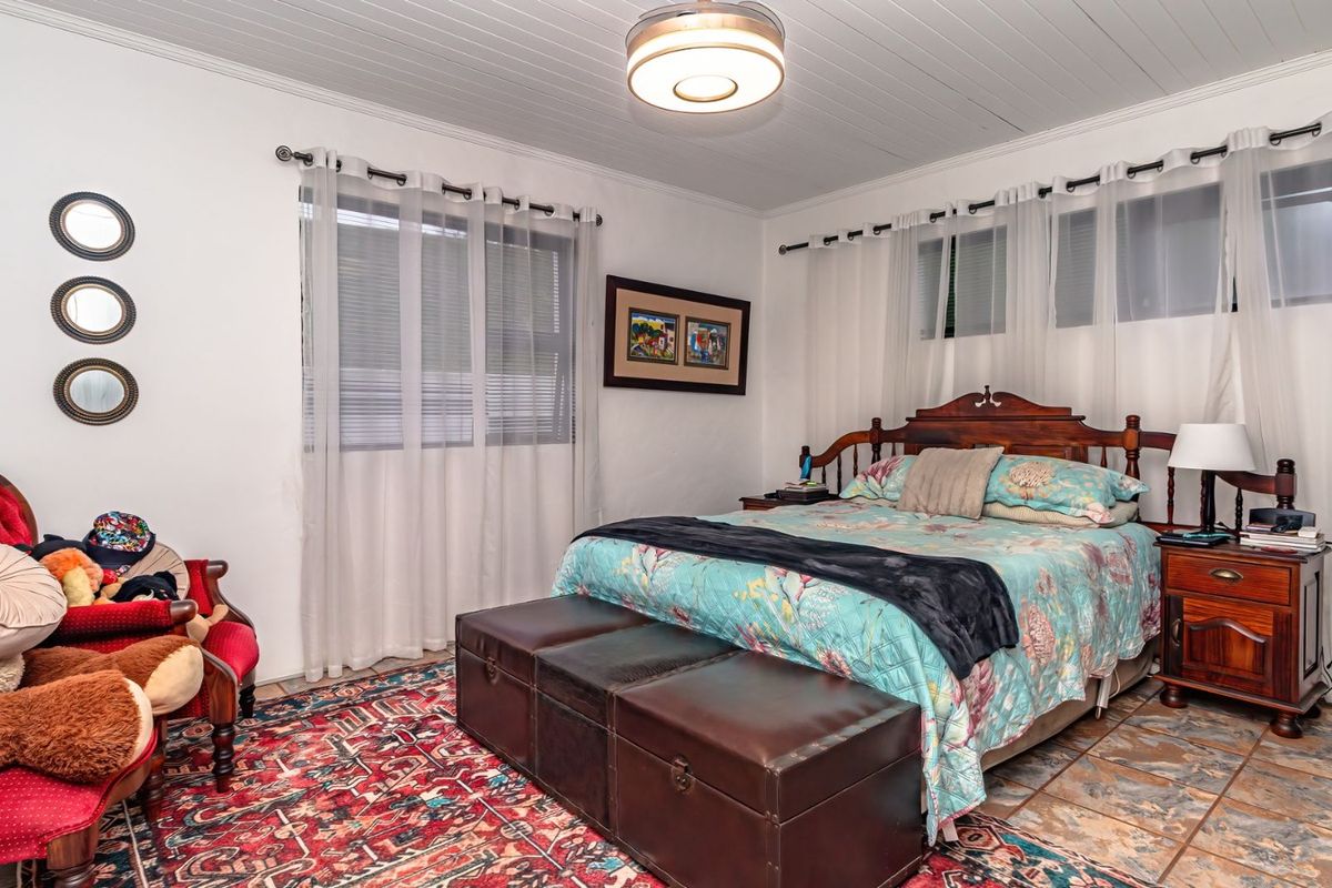 A bedroom featuring tiled flooring, a tongue and groove ceiling, and dual windows with sheer curtains.