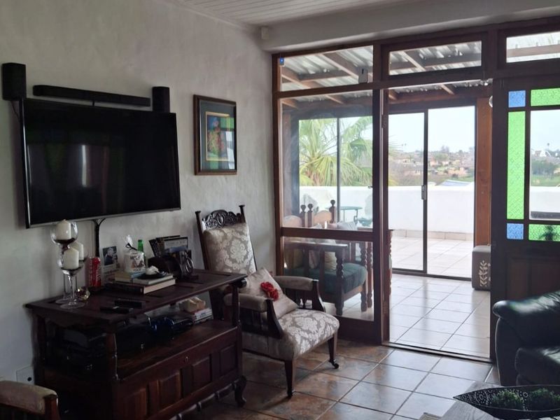 A living room featuring tiled flooring, a tongue and groove ceiling, and timber-framed sliding doors providing access to an outdoor patio area.