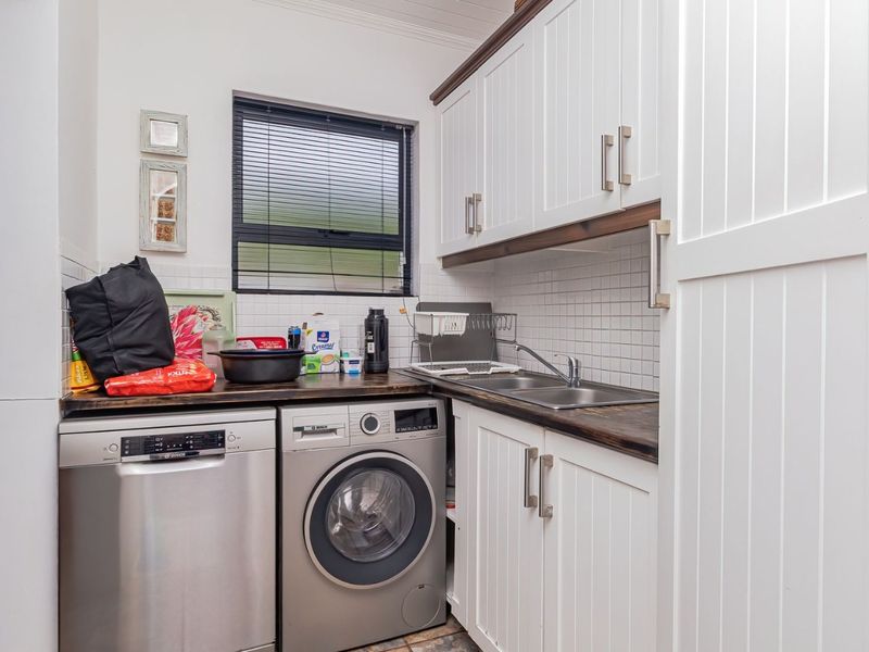 Compact laundry area featuring white cabinetry, dark laminate countertops, a stainless steel double sink, and tiled backsplash with space for under-counter appliances.