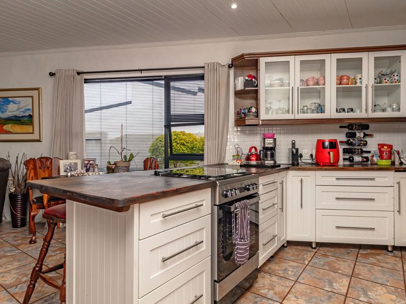 Open-plan kitchen featuring a central island with a cooktop, shaker-style cabinetry, glass-fronted wall units, and tiled flooring, seamlessly integrated with the living area.