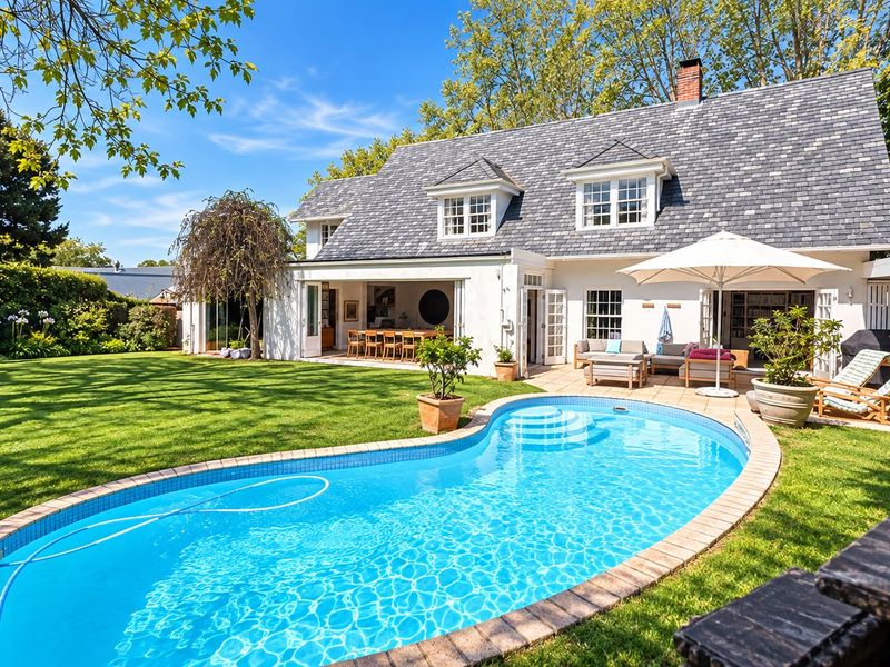 A beautifully maintained rear exterior featuring a swimming pool, paved patio area, and a classic home with a slate roof and dormer windows.