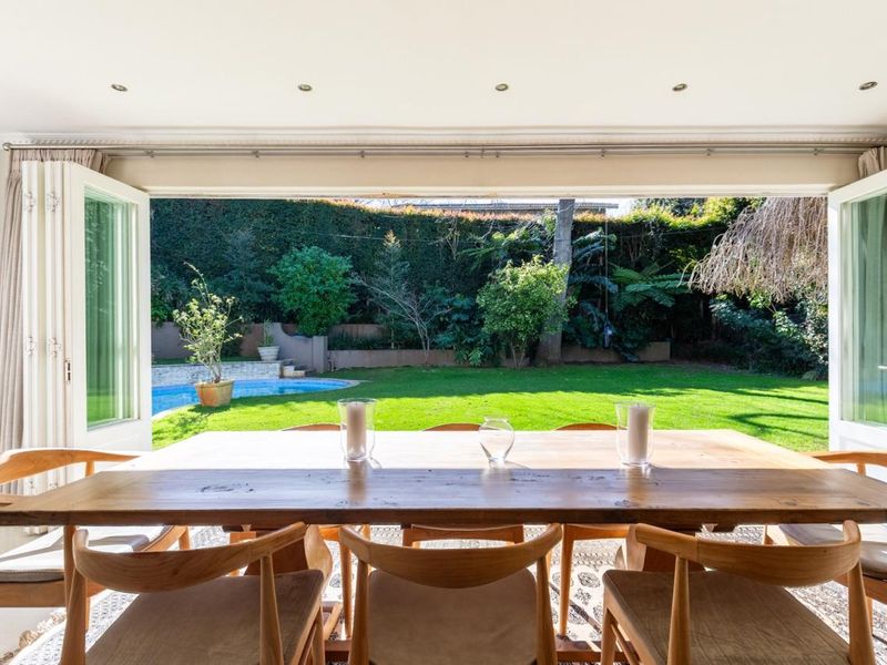 Dining area featuring large bi-fold doors that open onto a landscaped garden and swimming pool area, providing seamless indoor-outdoor flow.