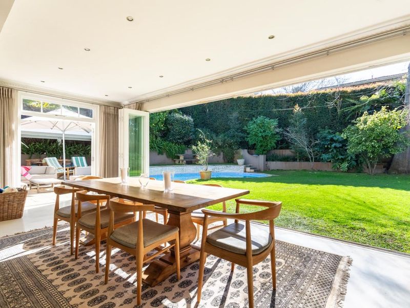 Bright open-plan dining area featuring seamless indoor-outdoor flow through large bi-fold doors leading to a private garden and swimming pool.