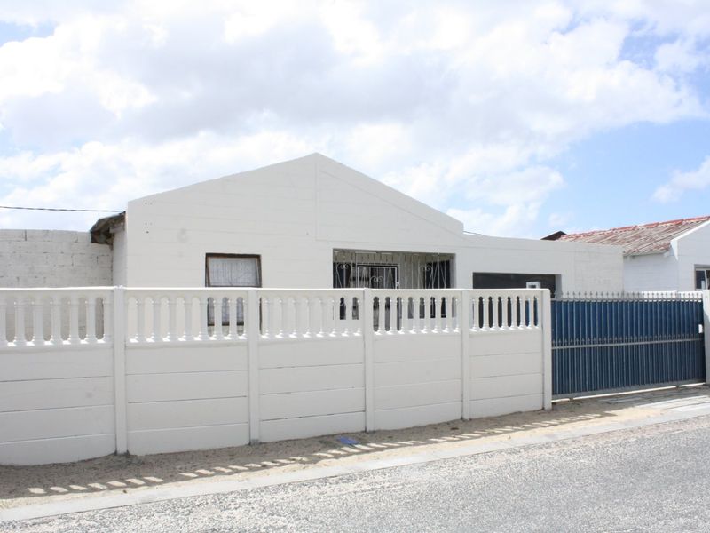 Front elevation of a single-story house featuring a precast concrete boundary wall, metal gate, and security bars on windows.