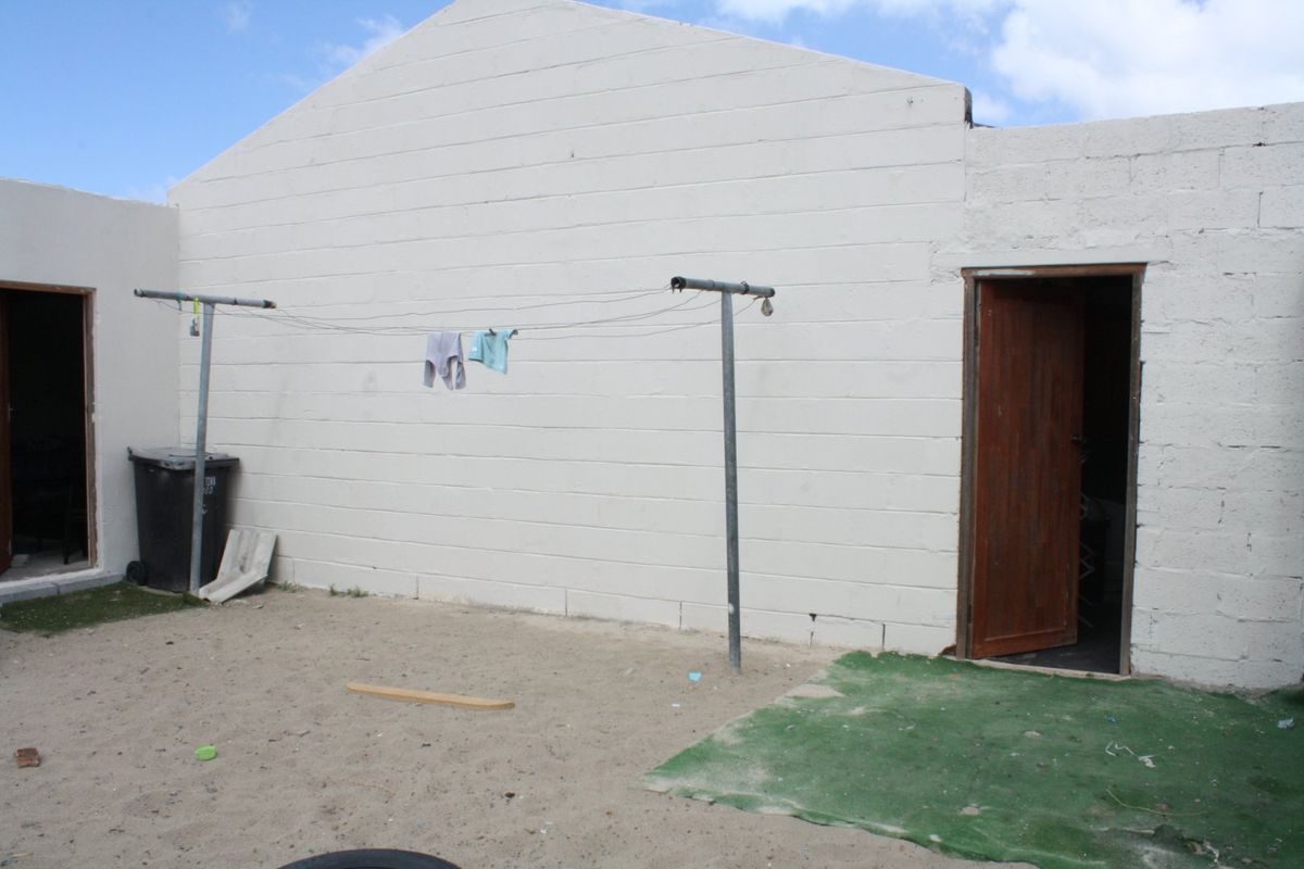Rear exterior view of the property featuring a painted concrete block wall, timber door access, and an open sandy yard area.
