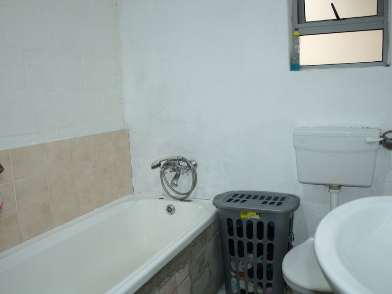 A functional bathroom featuring a bathtub with shower mixer, toilet, and basin, requiring cosmetic updates to the wall finishes and overall presentation.