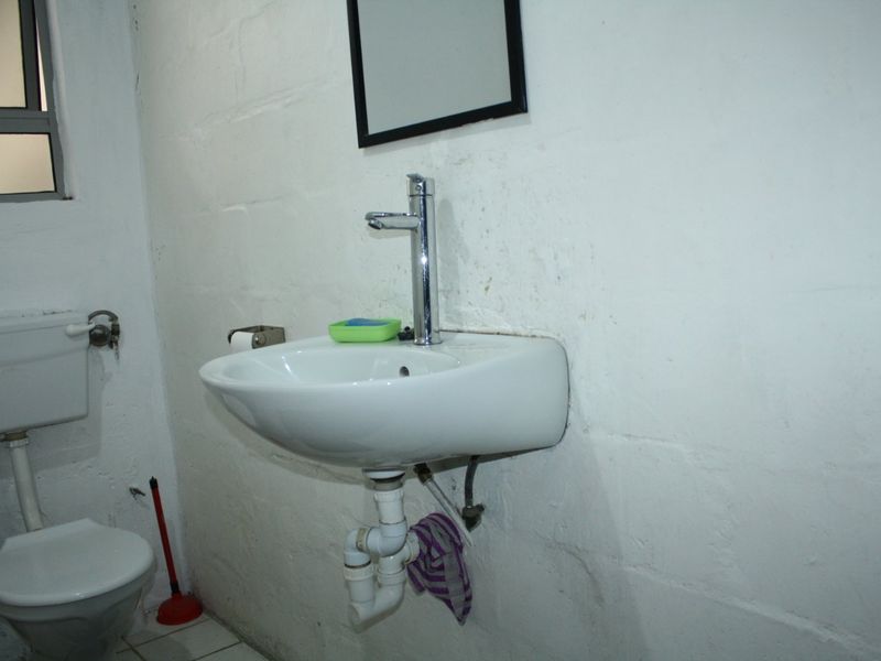 A functional bathroom featuring a wall-mounted basin with chrome mixer tap and a standard toilet, requiring cosmetic updates to the wall finishes.