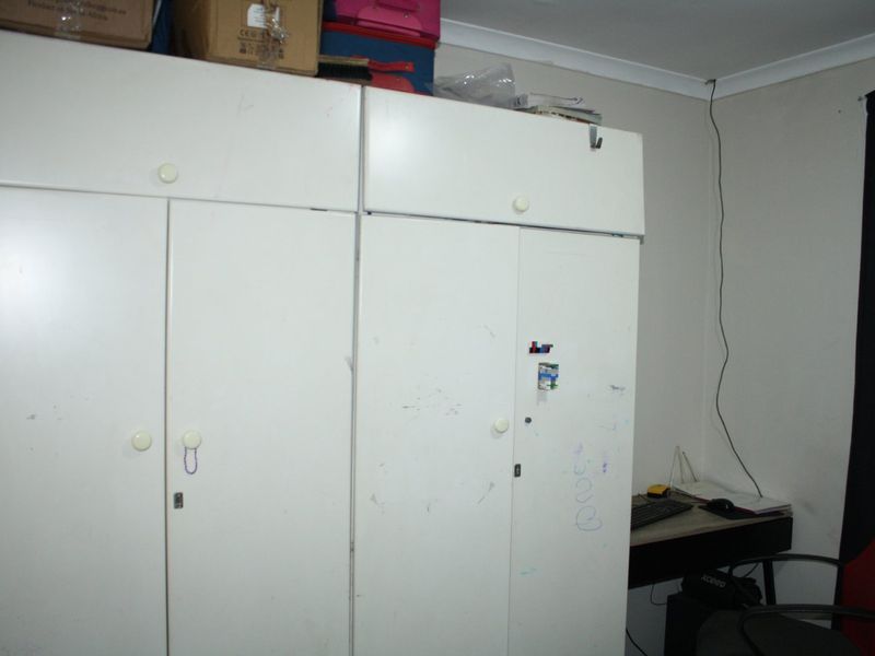 A bedroom featuring built-in white cupboards with visible surface wear and scuffing, requiring cosmetic attention.