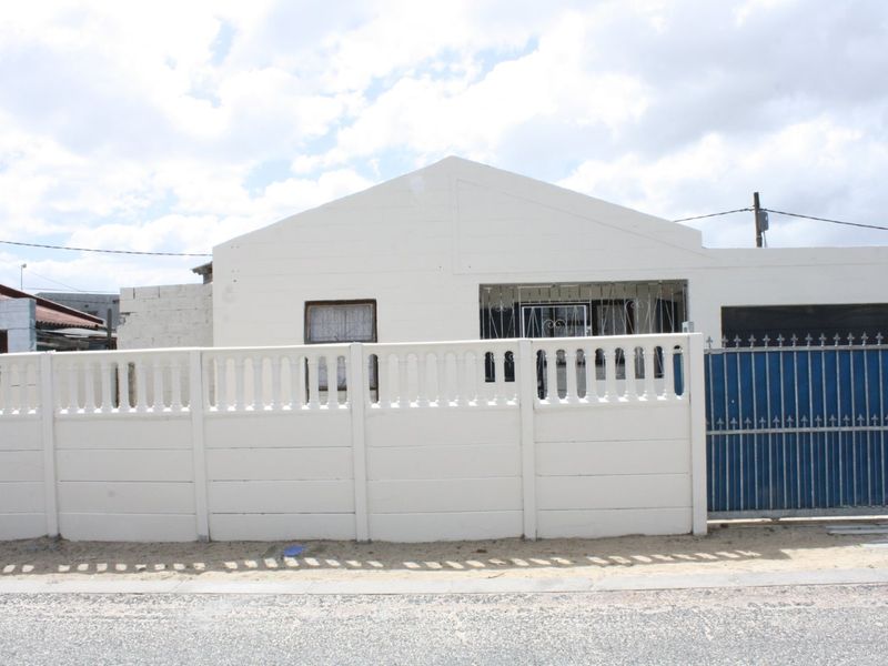 Front elevation of a single-story house featuring a white painted facade, secure metal gate, and a precast concrete boundary wall.