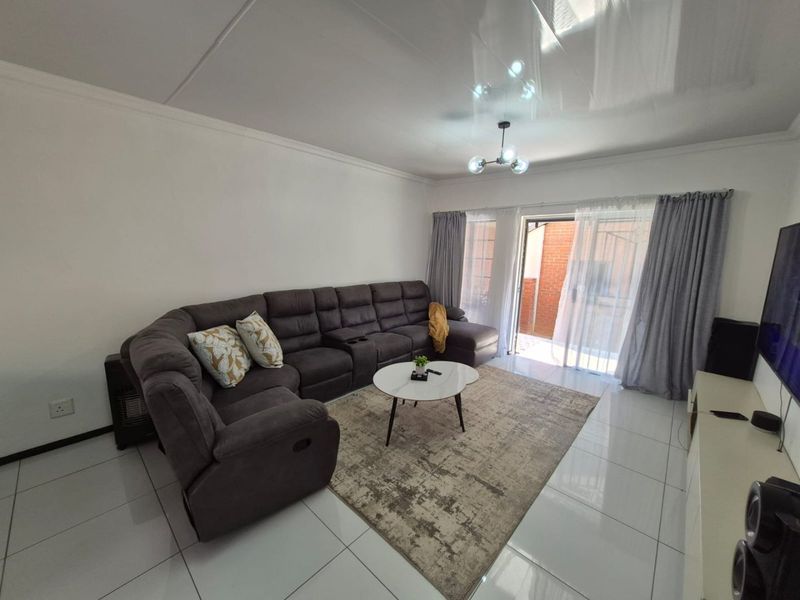 A bright and spacious living room featuring white tiled flooring, coved ceilings, and a sliding glass door providing access to the outdoor area.