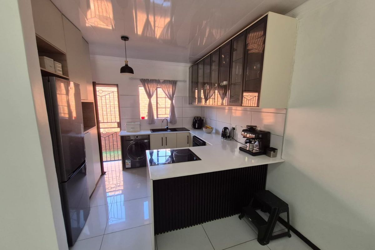 Modern kitchen featuring sleek cabinetry, quartz countertops, an integrated electric hob, and tiled flooring with direct access to the exterior.
