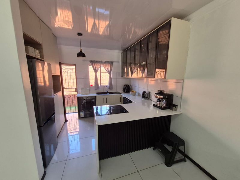 Modern kitchen featuring sleek cabinetry, quartz countertops, an integrated electric hob, and tiled flooring with direct access to the exterior.