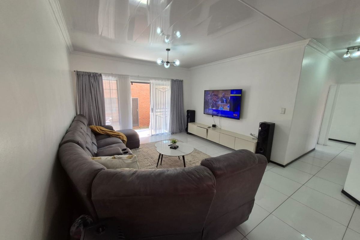 A bright and spacious living room featuring large format floor tiles, coved ceilings, and a sliding glass door providing access to the exterior.