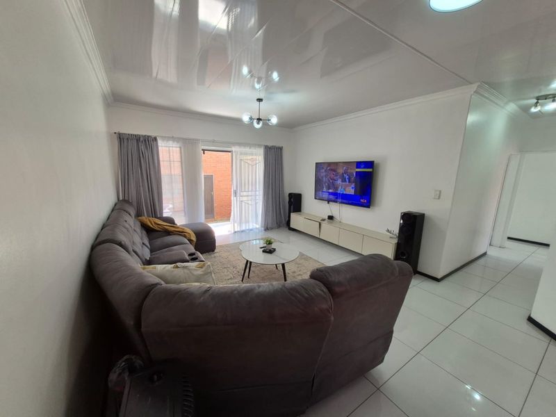 A bright and spacious living room featuring large format floor tiles, coved ceilings, and a sliding glass door providing access to the exterior.