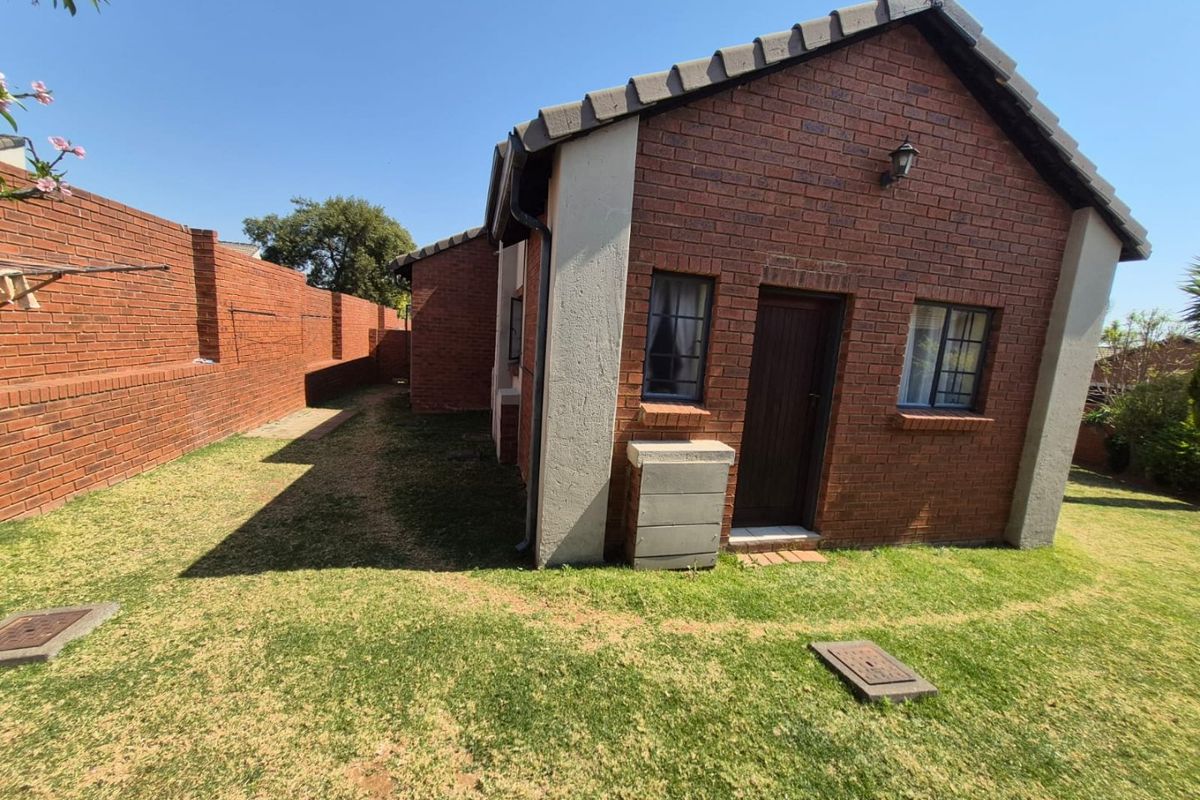 Rear view of a face brick townhouse featuring a private garden area with perimeter walling and established lawn.