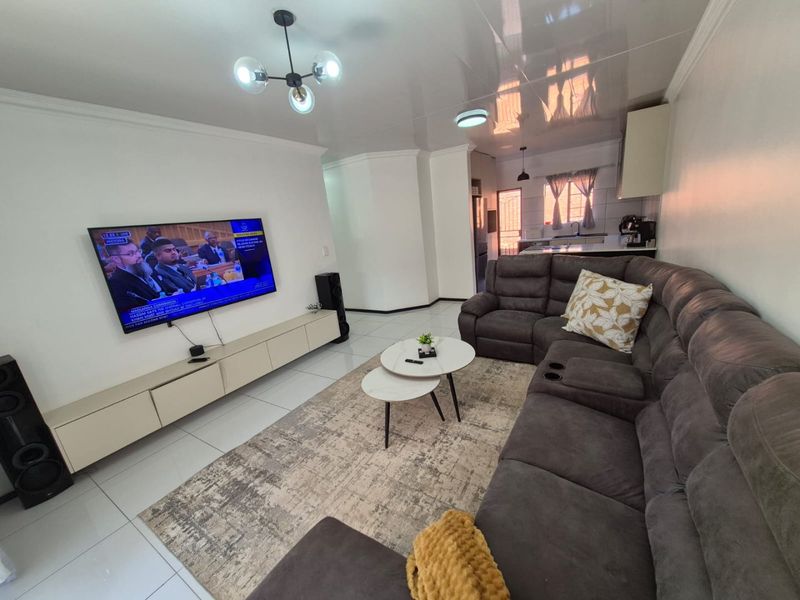 An open-plan living area featuring glossy ceilings, tiled floors, and a modern kitchen with built-in cabinetry and a sleek media console.