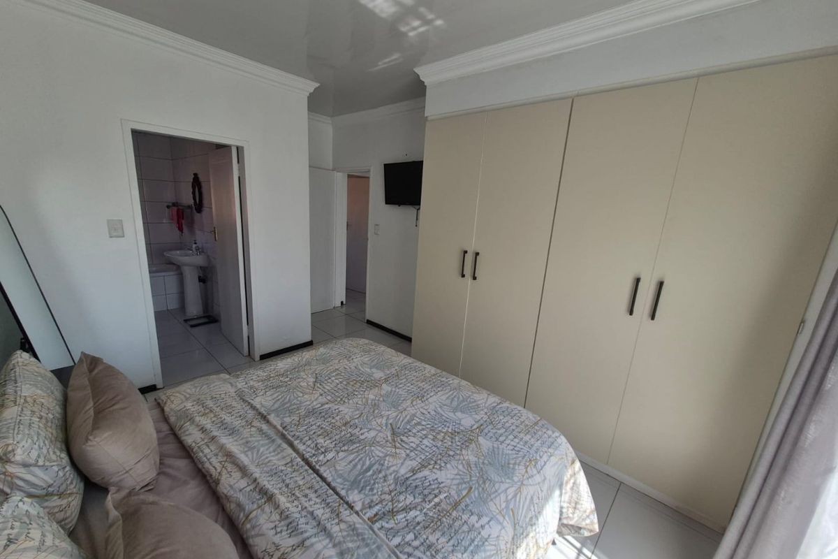 A well-maintained bedroom featuring built-in cupboards, tiled flooring, and direct access to an en-suite bathroom.