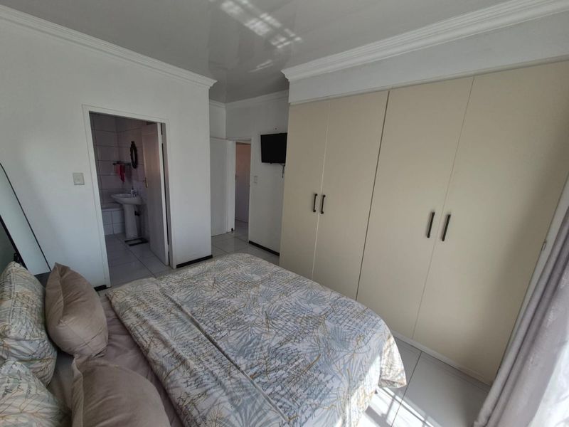 A well-maintained bedroom featuring built-in cupboards, tiled flooring, and direct access to an en-suite bathroom.