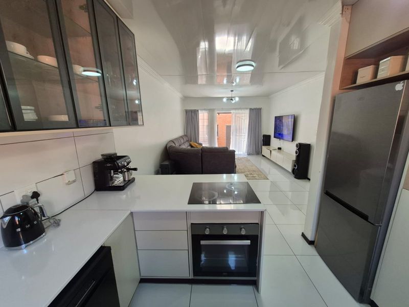Modern open-plan living area featuring a sleek kitchen with built-in appliances, glossy tiled floors, and seamless flow to the living space and outdoor access.