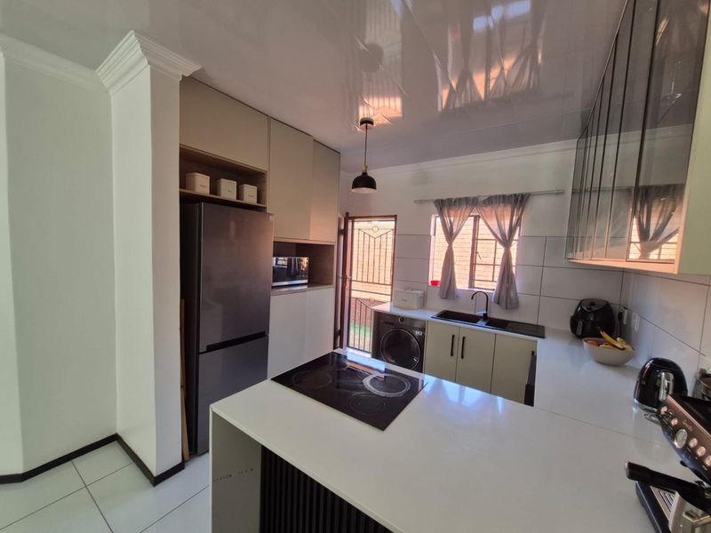 Modern kitchen featuring sleek cabinetry, quartz countertops, an integrated electric hob, and a double sink with direct access to the exterior.
