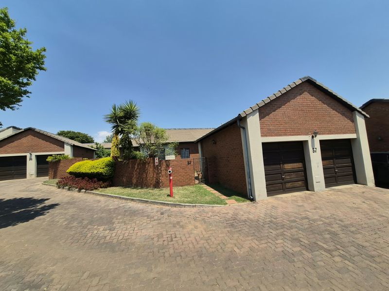 Front exterior view of a brick townhouse featuring a double garage, paved driveway, and established garden boundary wall.