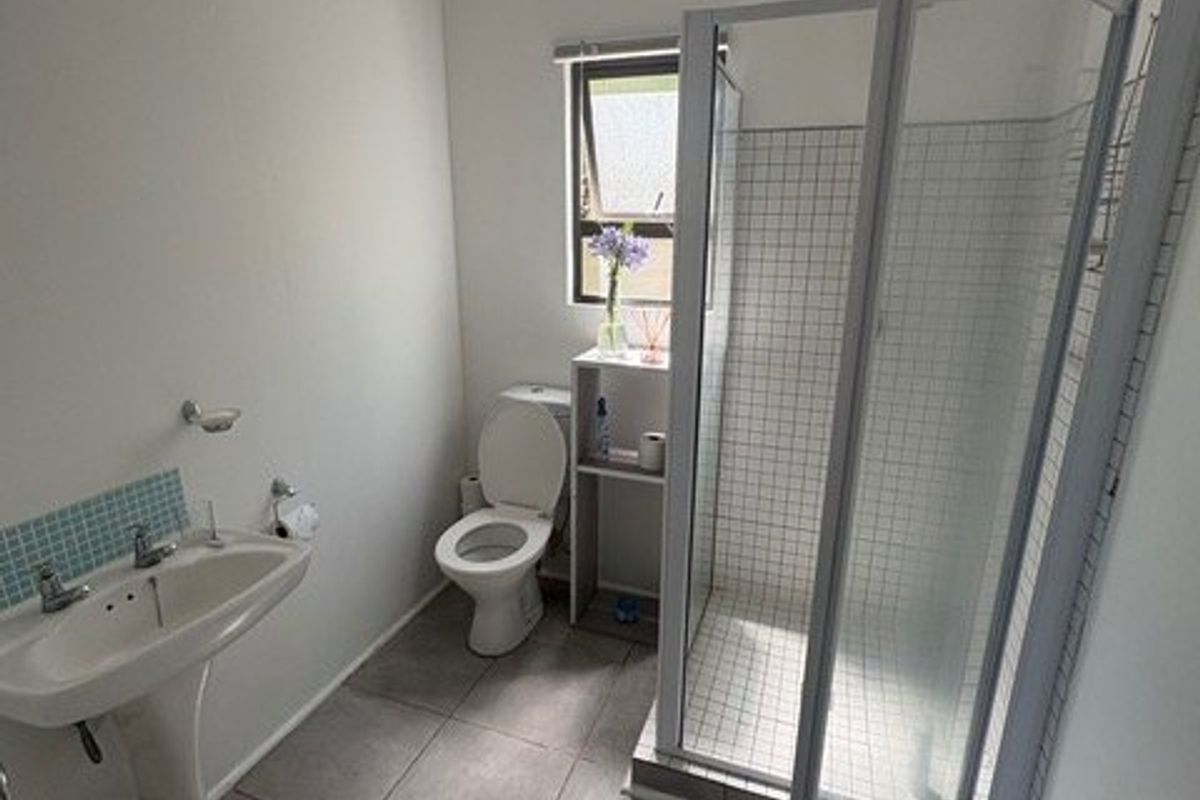 A functional bathroom featuring a pedestal washbasin, a toilet, and a glass-enclosed shower with tiled flooring and wall accents.