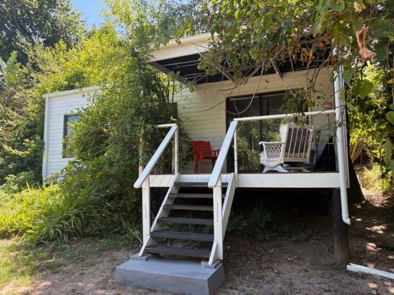 A raised timber deck with stairs and a roof overhang, providing outdoor access to the home, surrounded by mature garden vegetation.