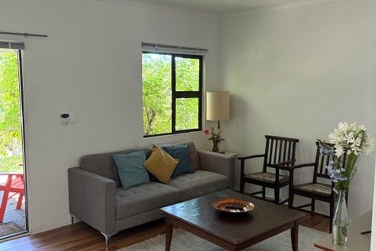 A comfortable living room featuring laminate flooring, natural light from a large window, and direct access to an outdoor area through a sliding glass door.