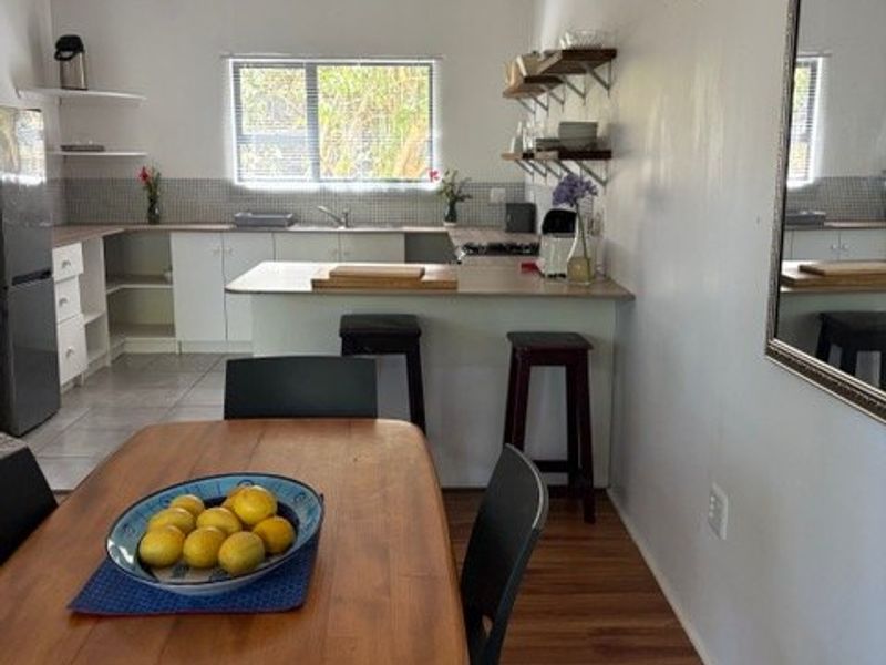 Open plan kitchen and dining area featuring laminate flooring, white cabinetry, tiled backsplash, and a breakfast bar counter.