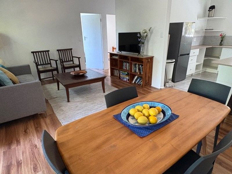 Open plan living and dining area featuring laminate flooring and an adjacent kitchen with built-in cabinetry and open shelving.