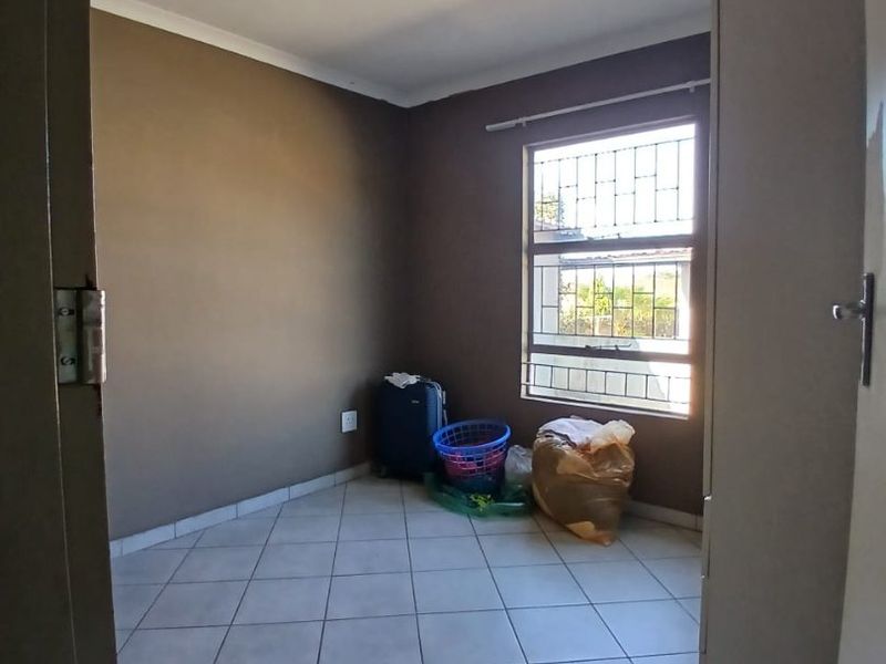 A simple, empty bedroom featuring tiled flooring and a window fitted with security bars, offering a neutral canvas for potential updates.
