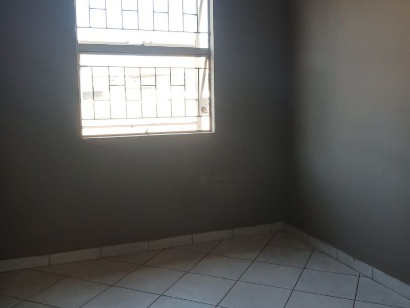 An empty bedroom featuring neutral grey walls, tiled flooring, and a window fitted with security bars.
