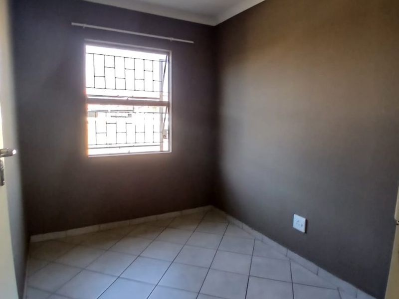 A vacant bedroom featuring tiled flooring, dark painted walls, and a window fitted with security bars.