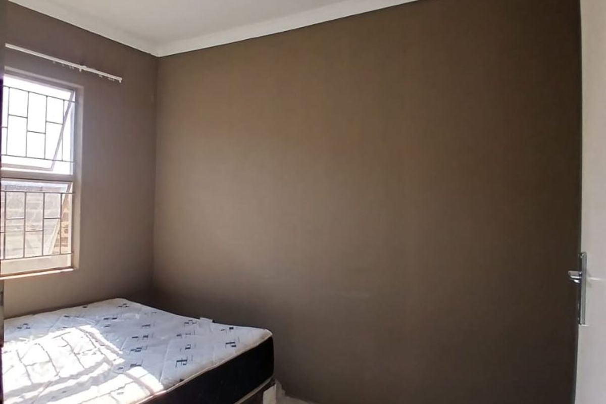 A compact bedroom featuring tiled flooring, a window with security bars, and a ceiling-mounted light fixture.